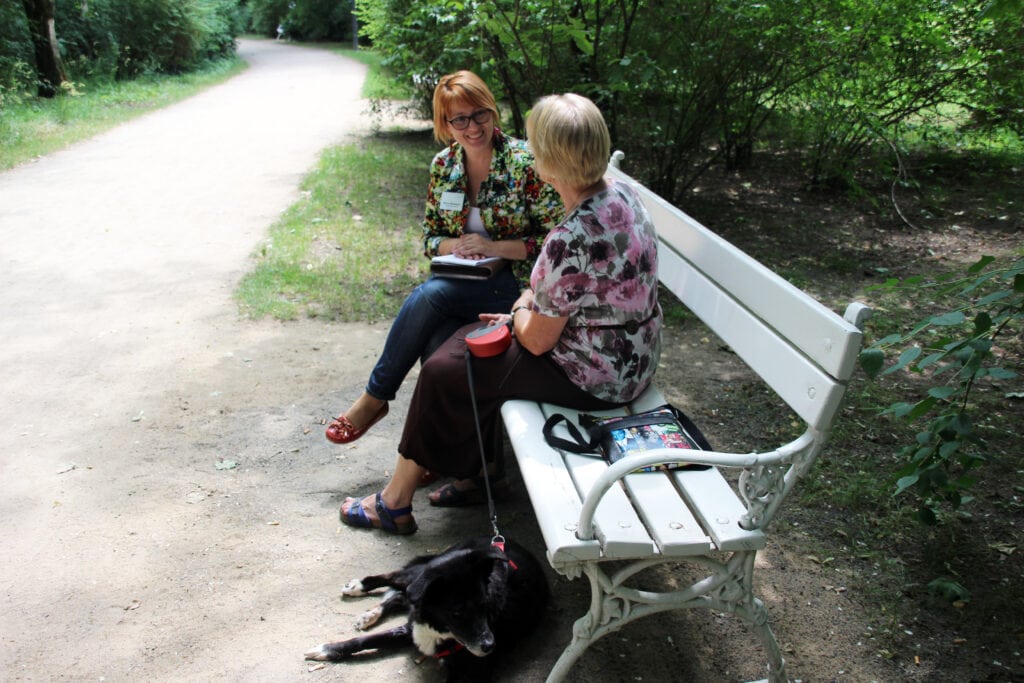 Zwei Frauen unterhalten sich mit Hund auf Parkbank