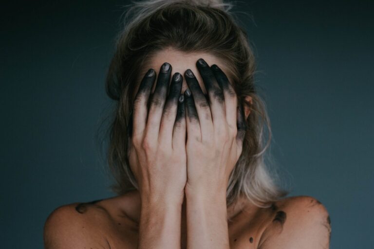 Frau schlägt schwarz gefärbte Hände vor dem Gesicht zusammen
