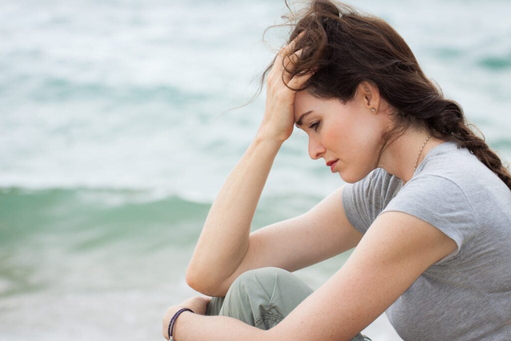 Frau sitzt verzweifelt mit Hand am Kopf am Meer