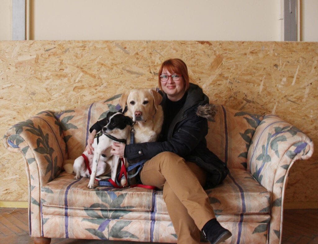 Frau kuschelt mit zwei Hunden auf einem alten Sofa
