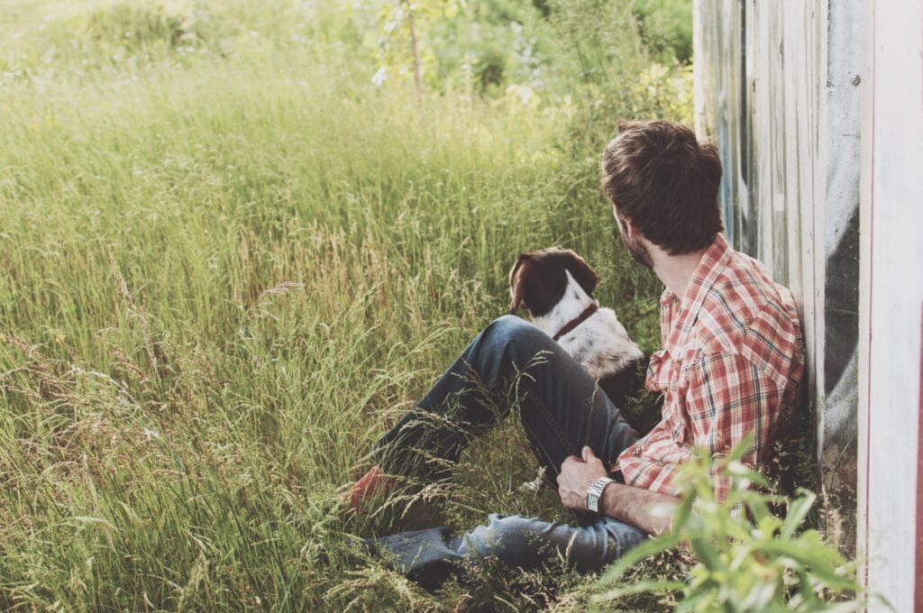 Mann sitzt mit Hund im Gras