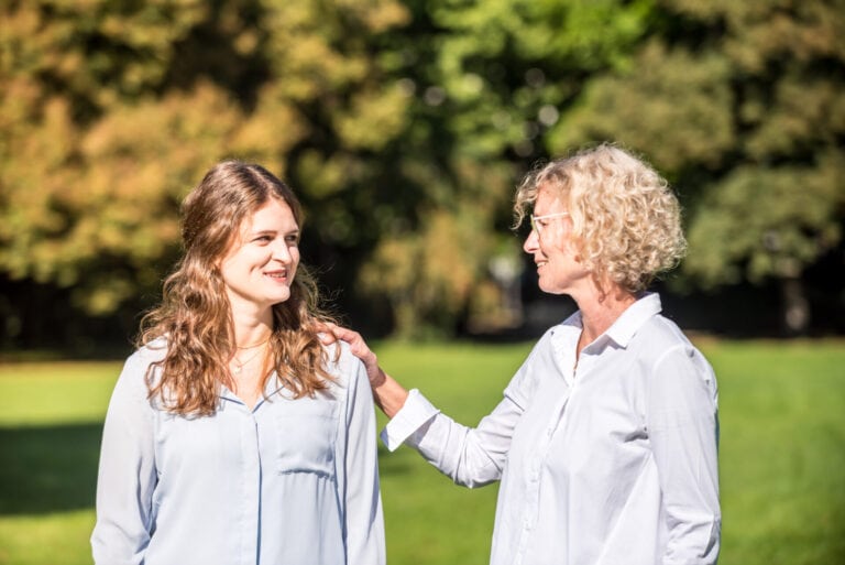 Frau fasst einer anderen Frau an die Schulter und lächelt