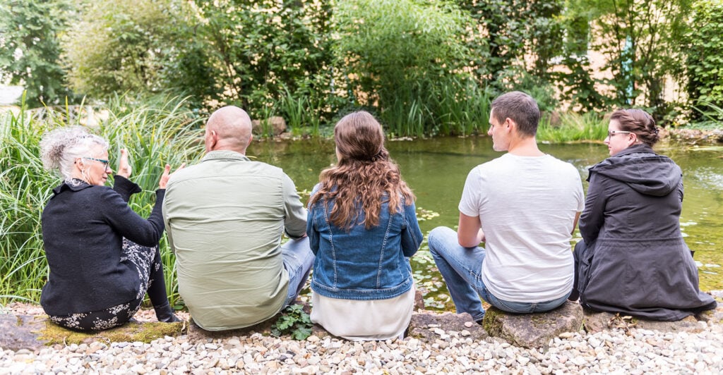 5 Personen sitzen nebeneinander und Unterhalten sich am Fluss