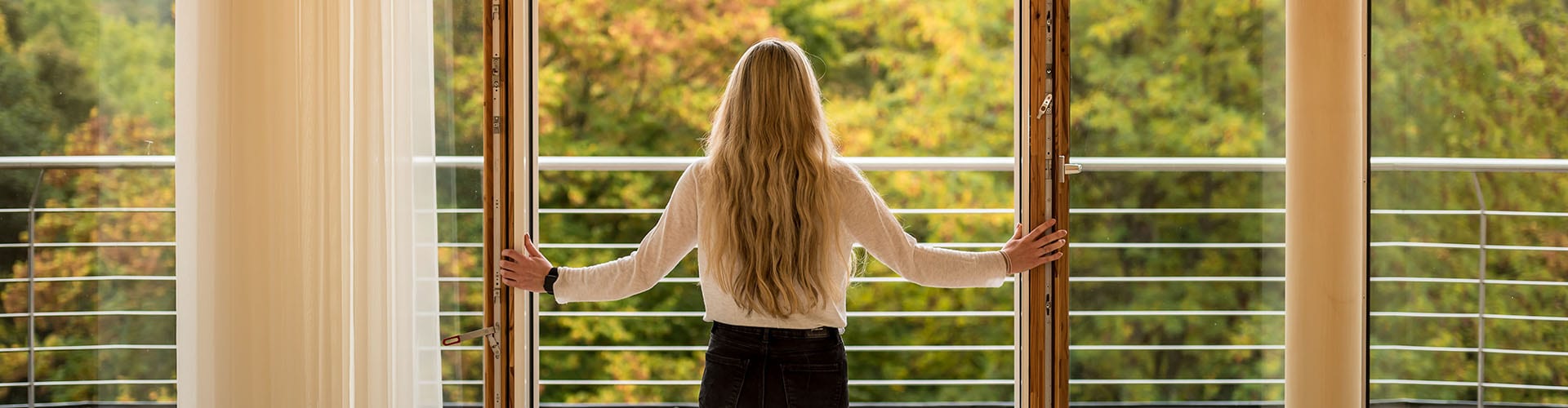 Post-Covid - Frau, die aus einem offenen Fenster in die Natur schaut