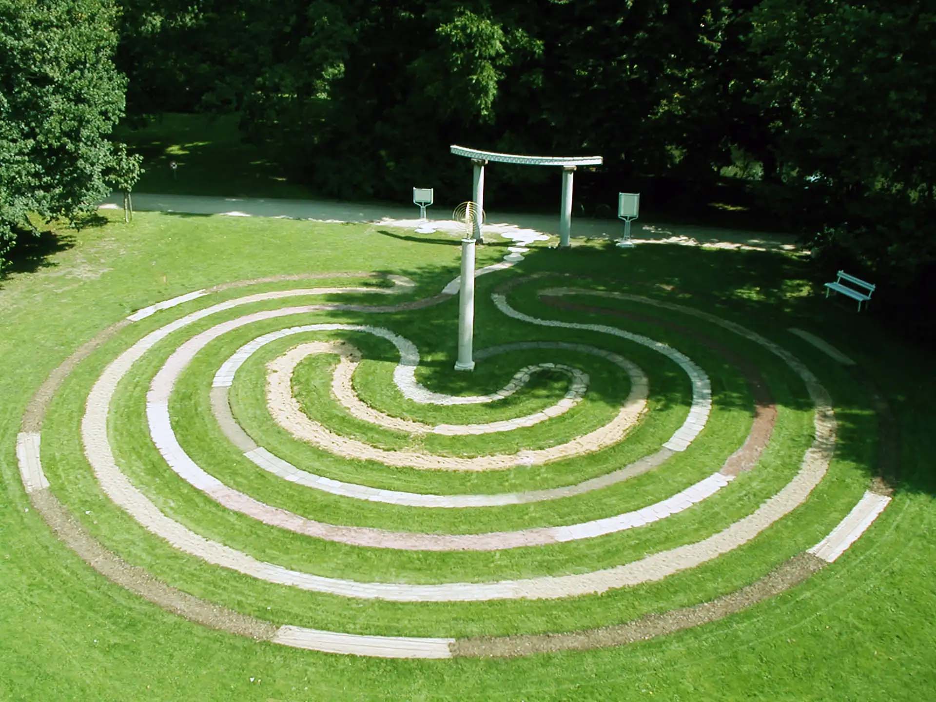 Kreisfoermiges Parklabyrinth in gruener Umgebung mit zentralem Steintor.