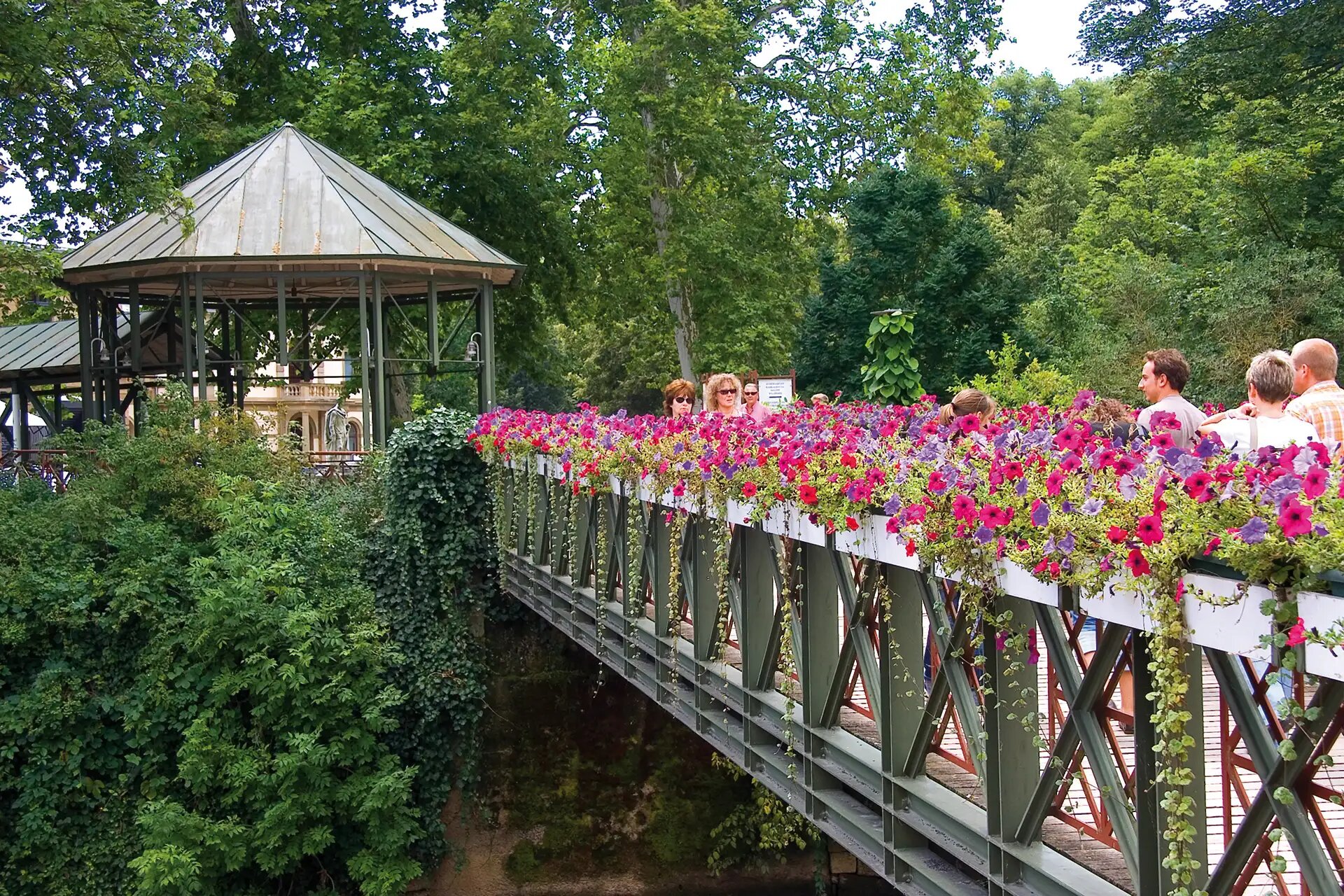 Blumenverzierte Bruecke mit Menschen in einem gruenen Park in Bad Kissingen.