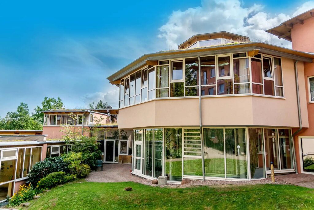 Moderne Klinik mit großen Fenstern und Garten, blauer Himmel im Hintergrund.