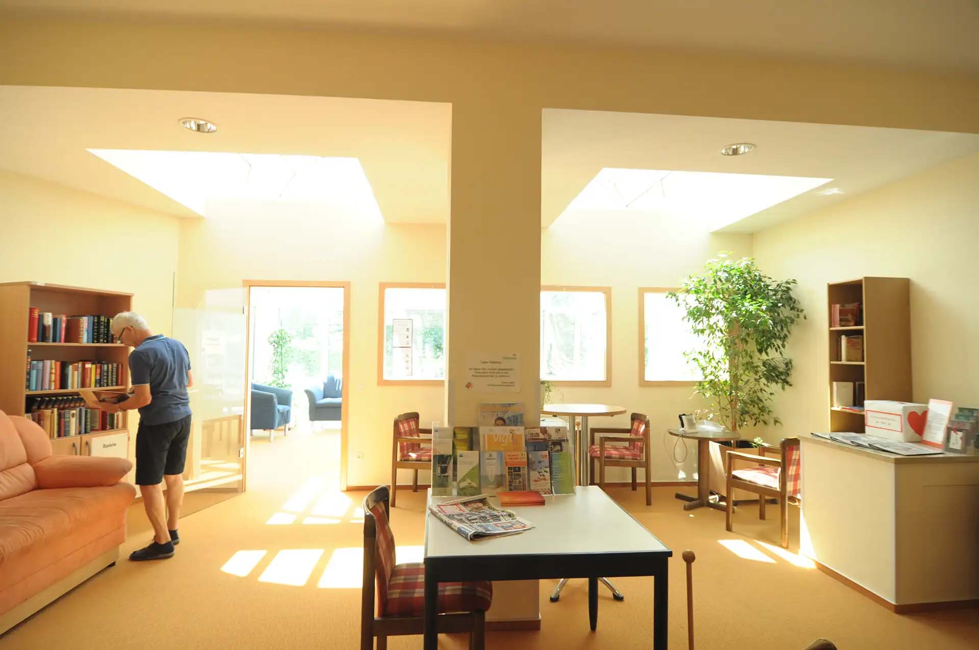 Heller Raum mit Buecherregalen, Tischen, Pflanzen und Sitzgelegenheiten.