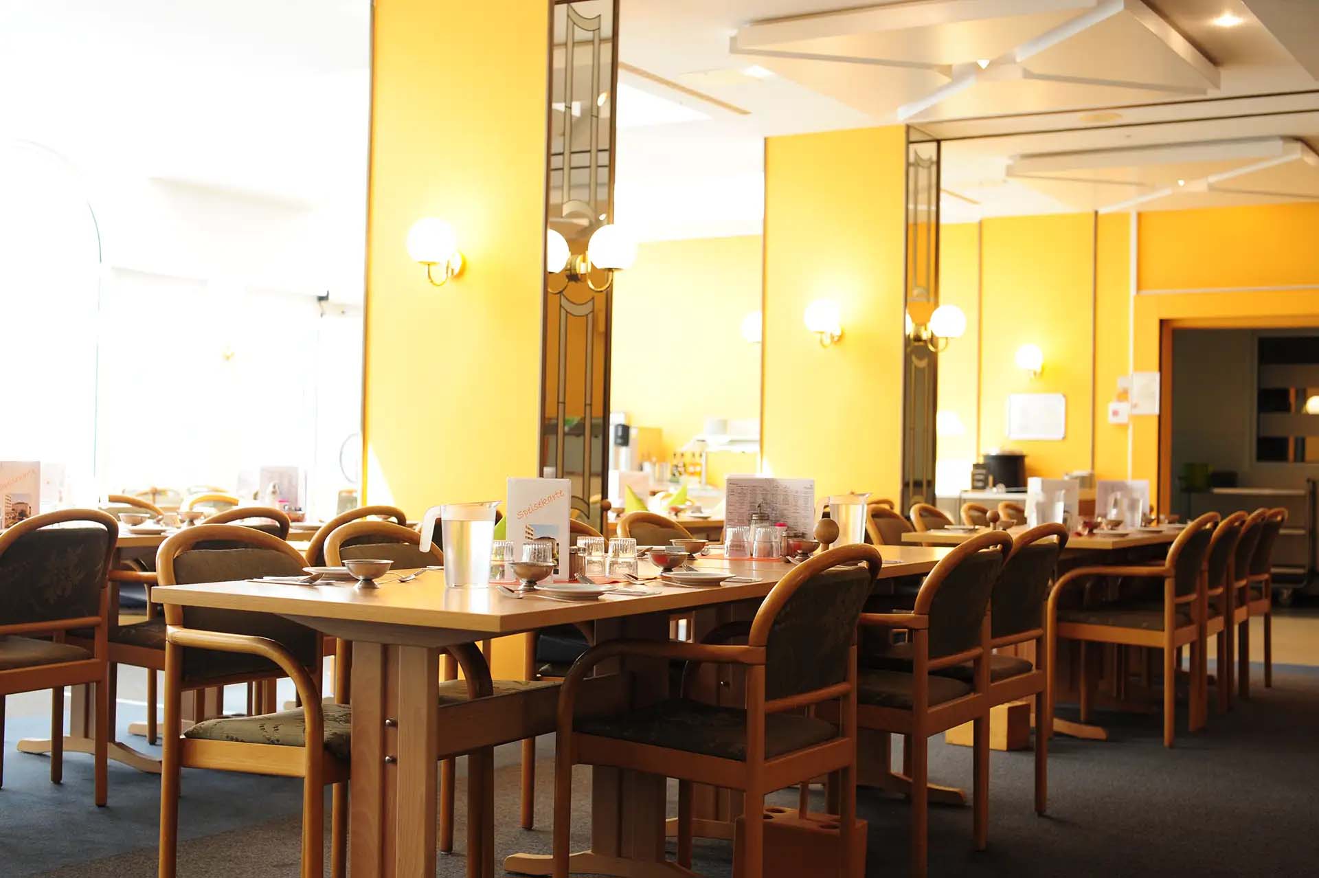 Gemuetlicher Speisesaal mit gedeckten Tischen in warmen Gelbtoenen.