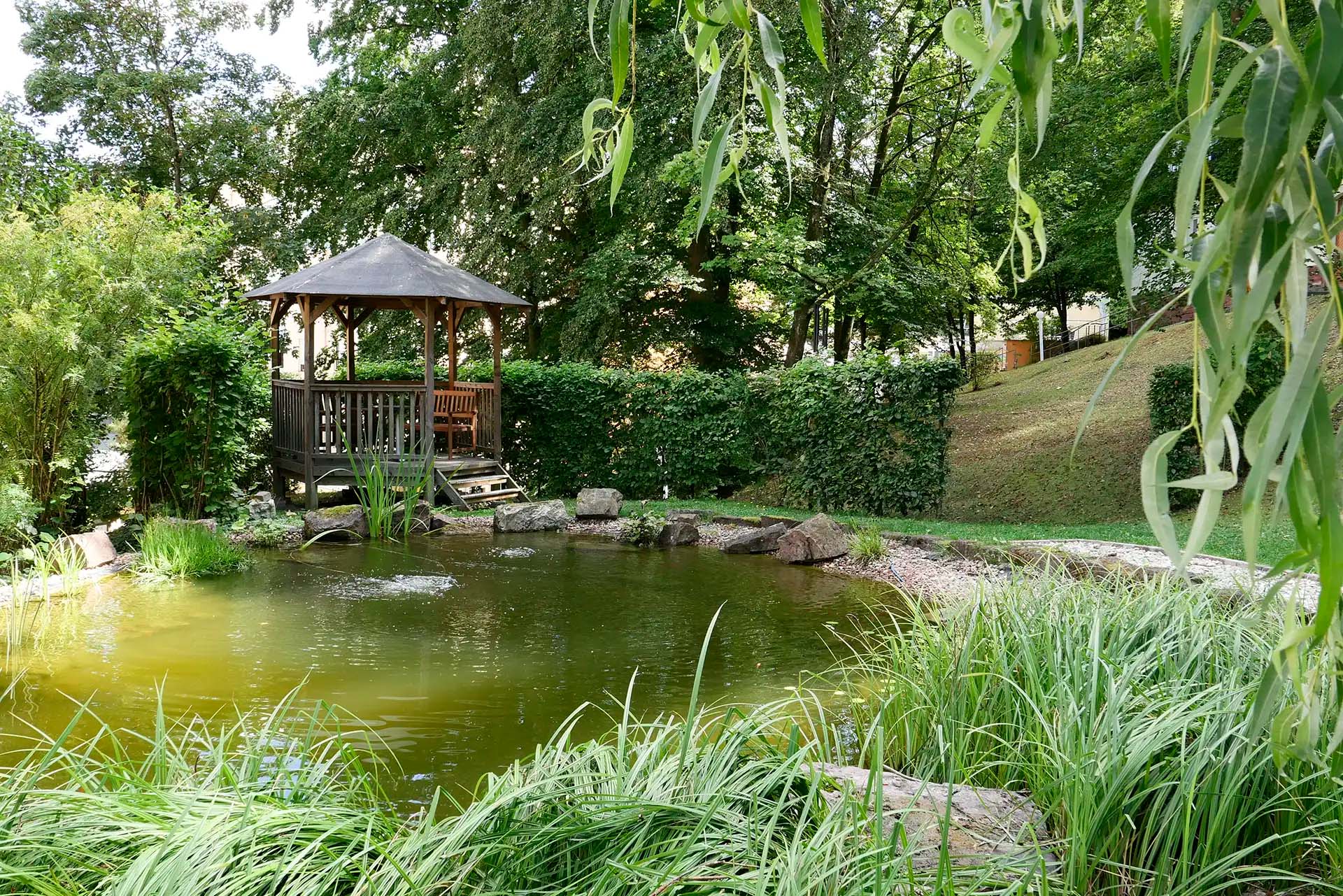 Ein Pavillon am Teich im Garten mit ueppiger Vegetation.