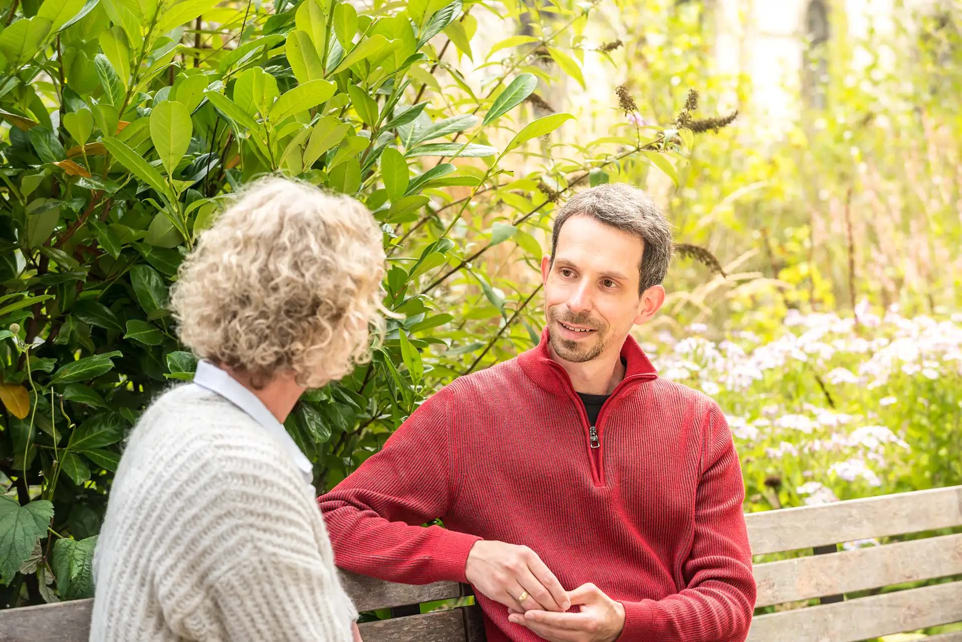 Zwei Menschen sitzen auf einer Bank und unterhalten sich im Garten.