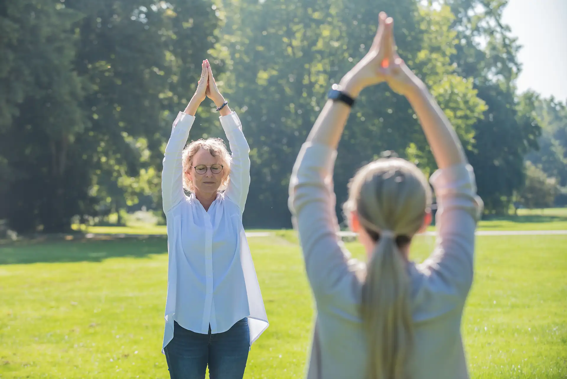 Zwei Personen machen gemeinsam Yoga-Uebungen im Gruenen.