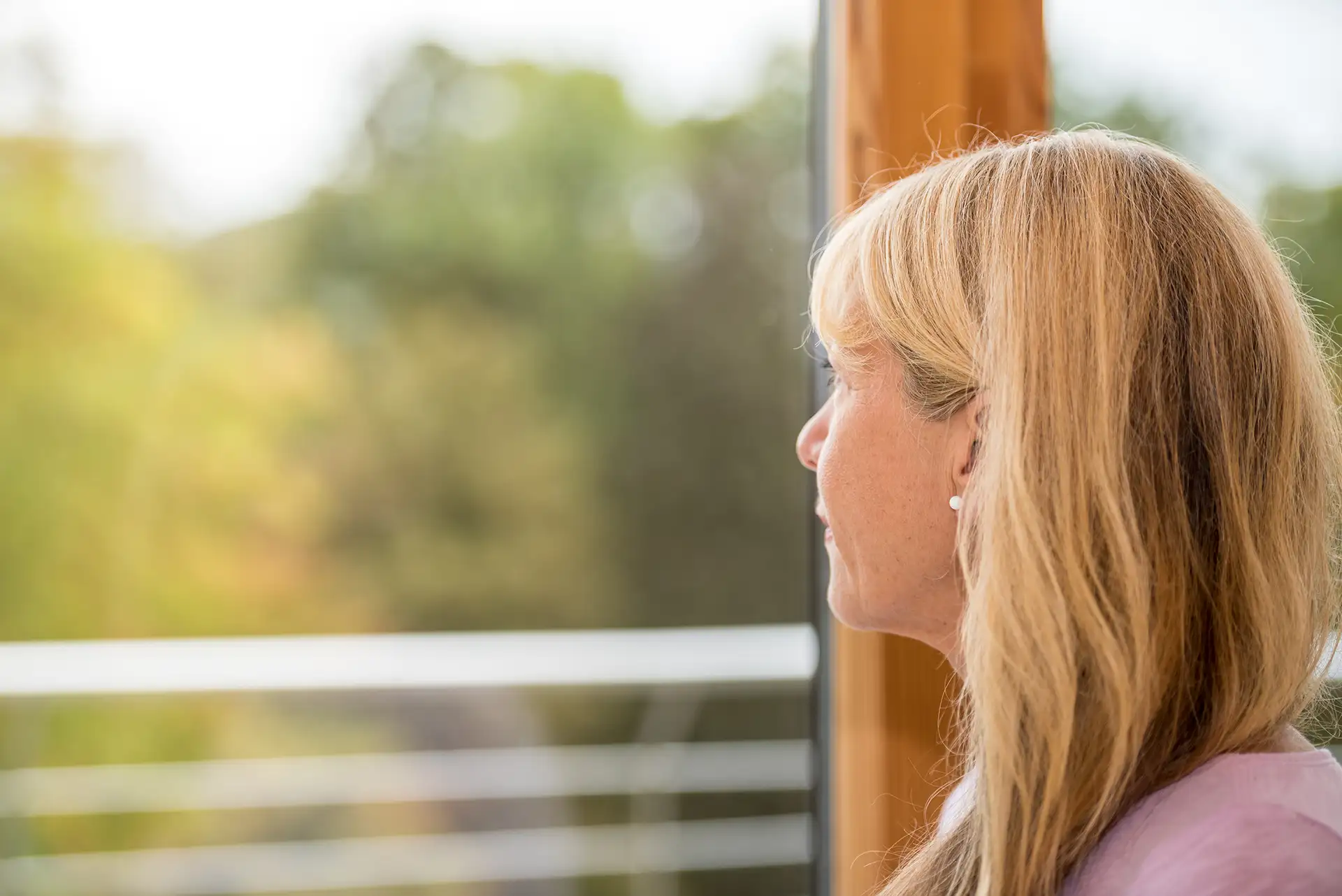 Frau schaut nachdenklich aus einem Fenster in die Natur.