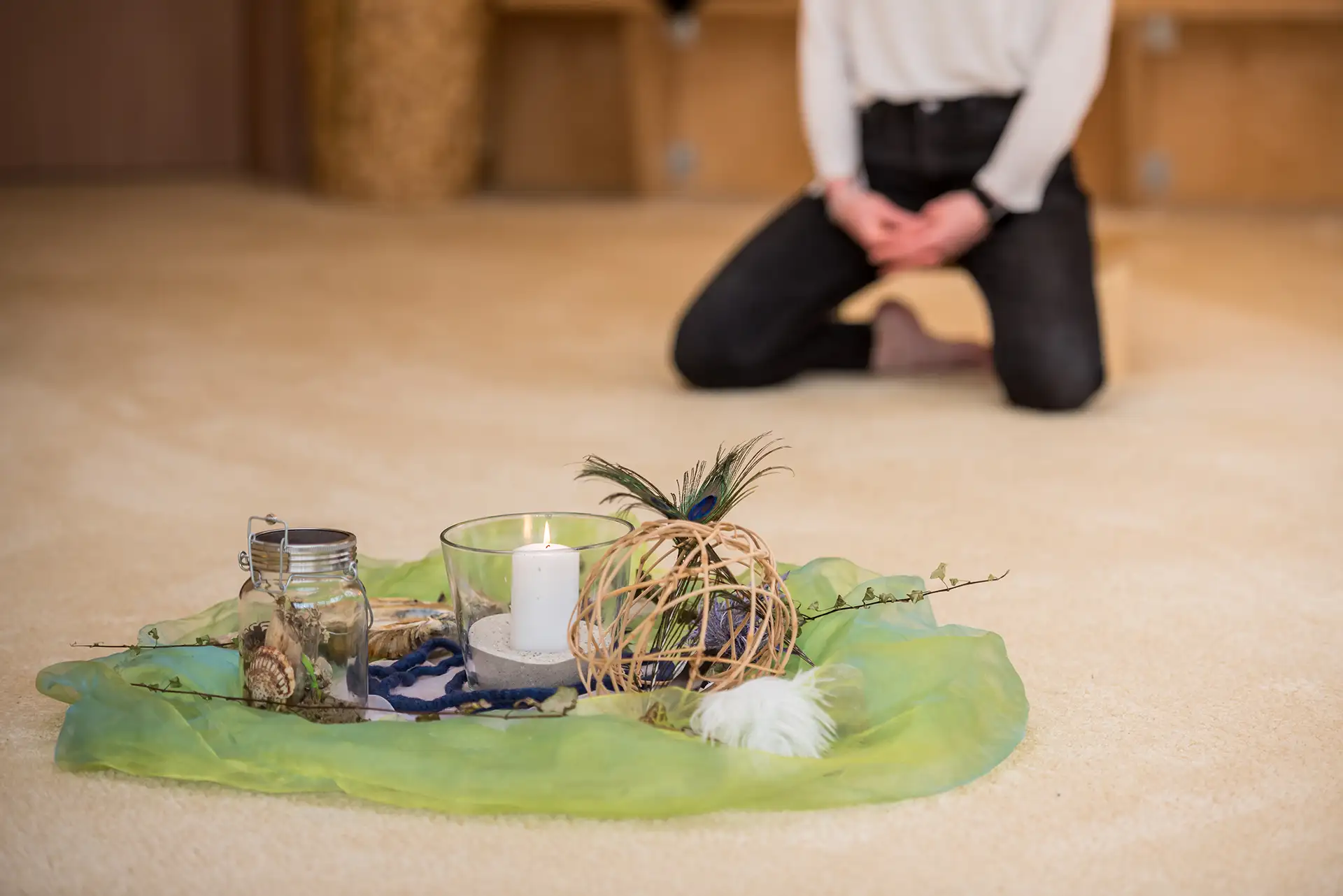 Frau kniet vor einem Meditationsaltar mit Kerze, Federn und Dekorationen.