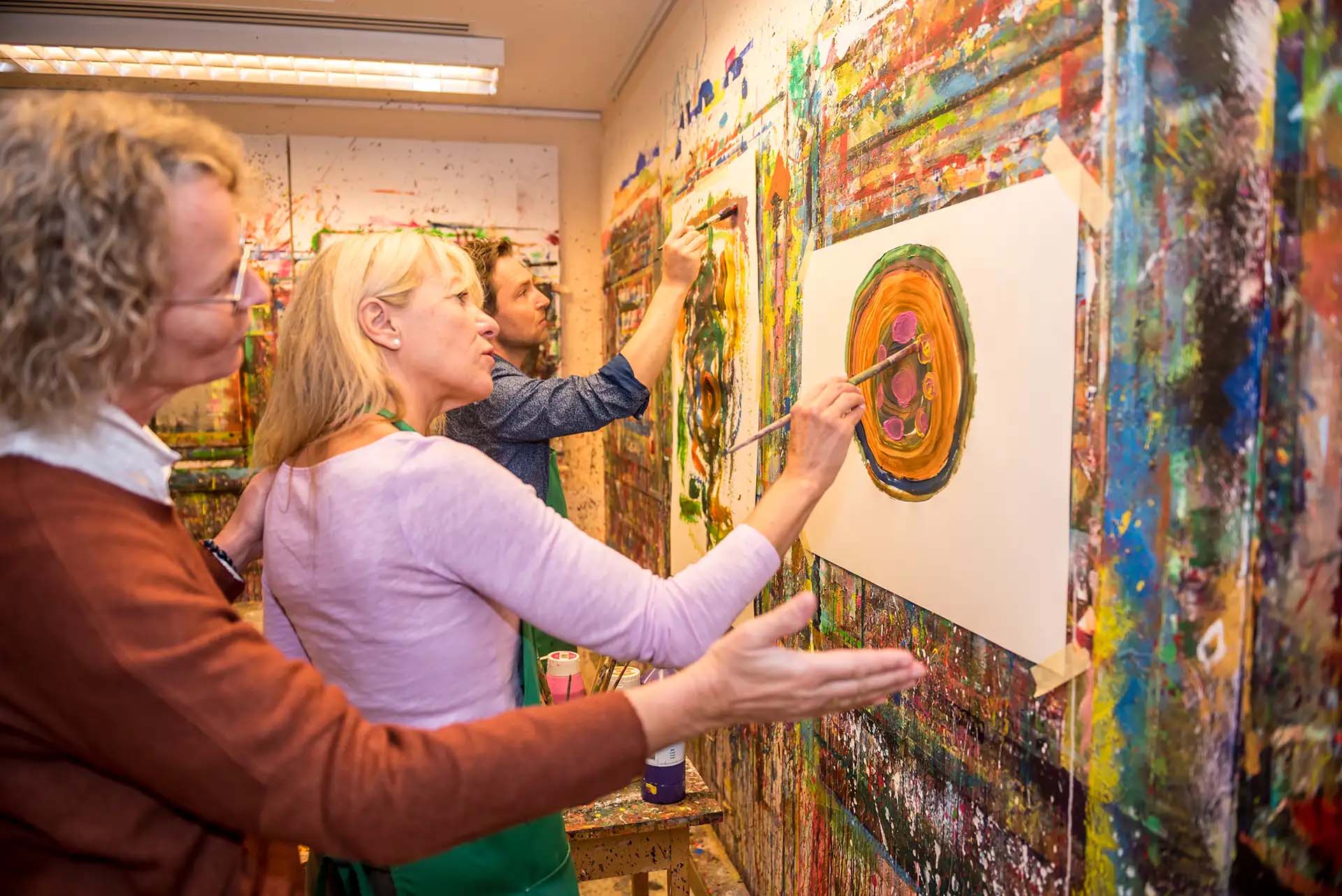 Menschen malen zusammen an einer farbenfrohen Wand bei einer Maltherapiesitzung.