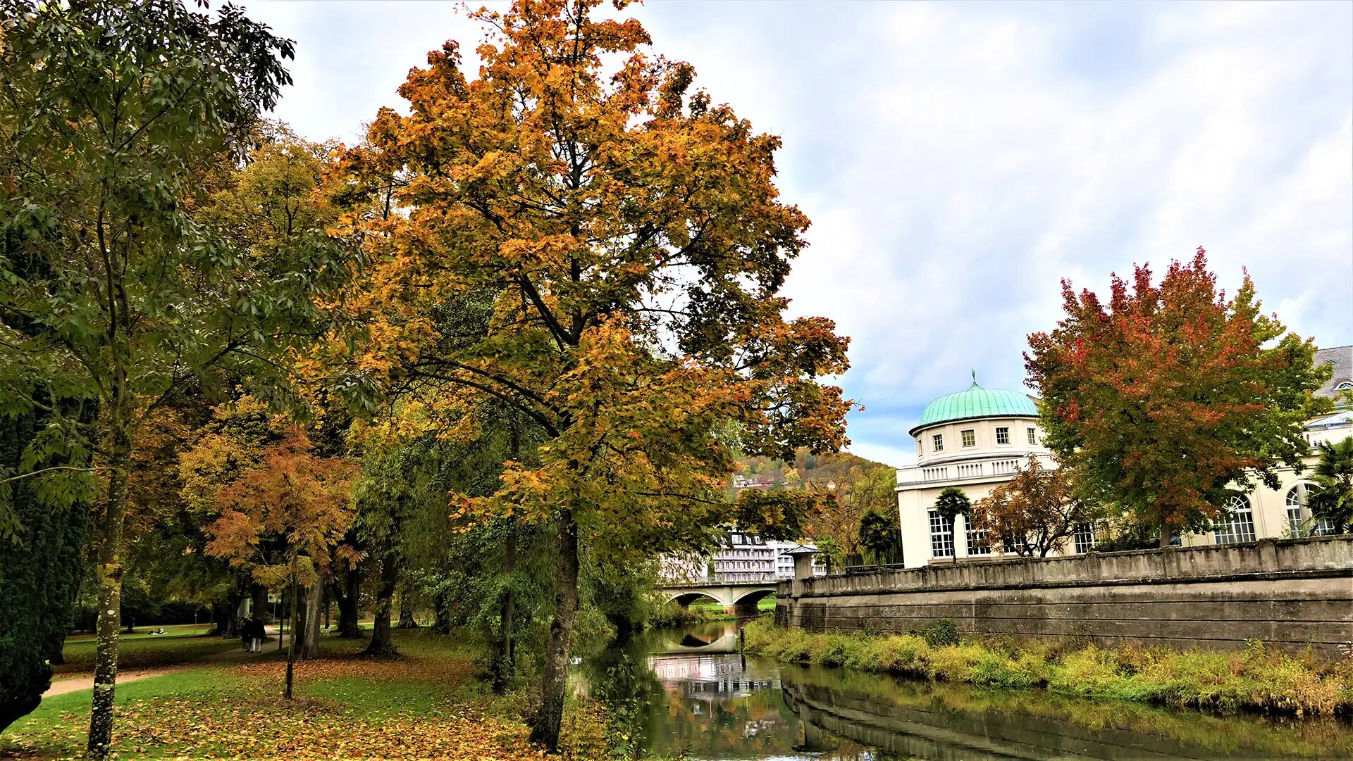 Herbstlicher Park in Bad Kissingen mit Fluss und historischen Gebäuden.