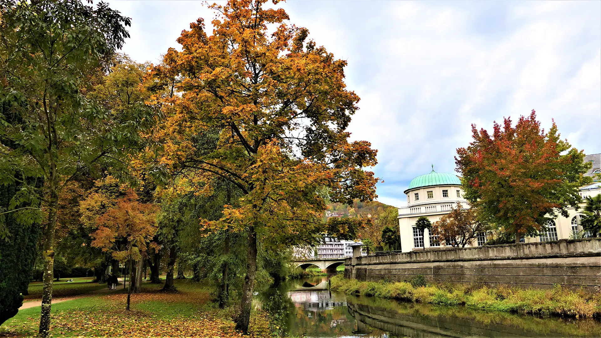 Herbstlicher Park in Bad Kissingen mit Fluss und historischen Gebäuden.