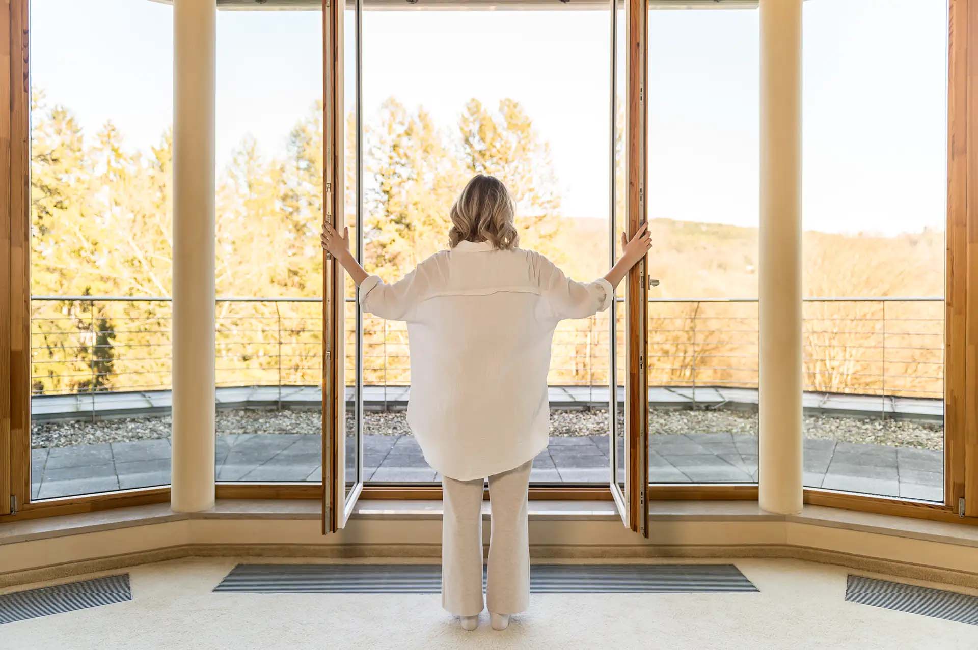Person oeffnet Tueren mit Blick auf eine sonnige Herbstlandschaft.