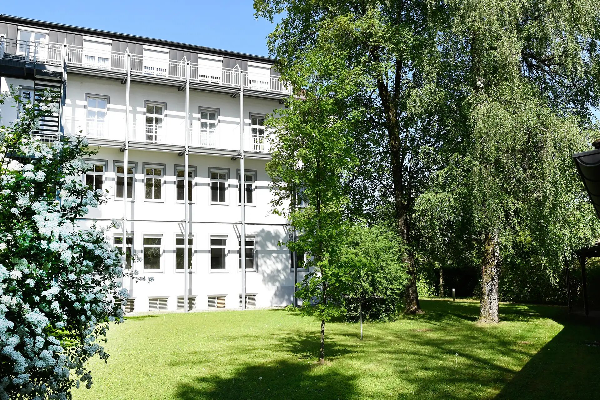 Rückansicht des Hauses mit grünem Garten und blühenden Bäumen.