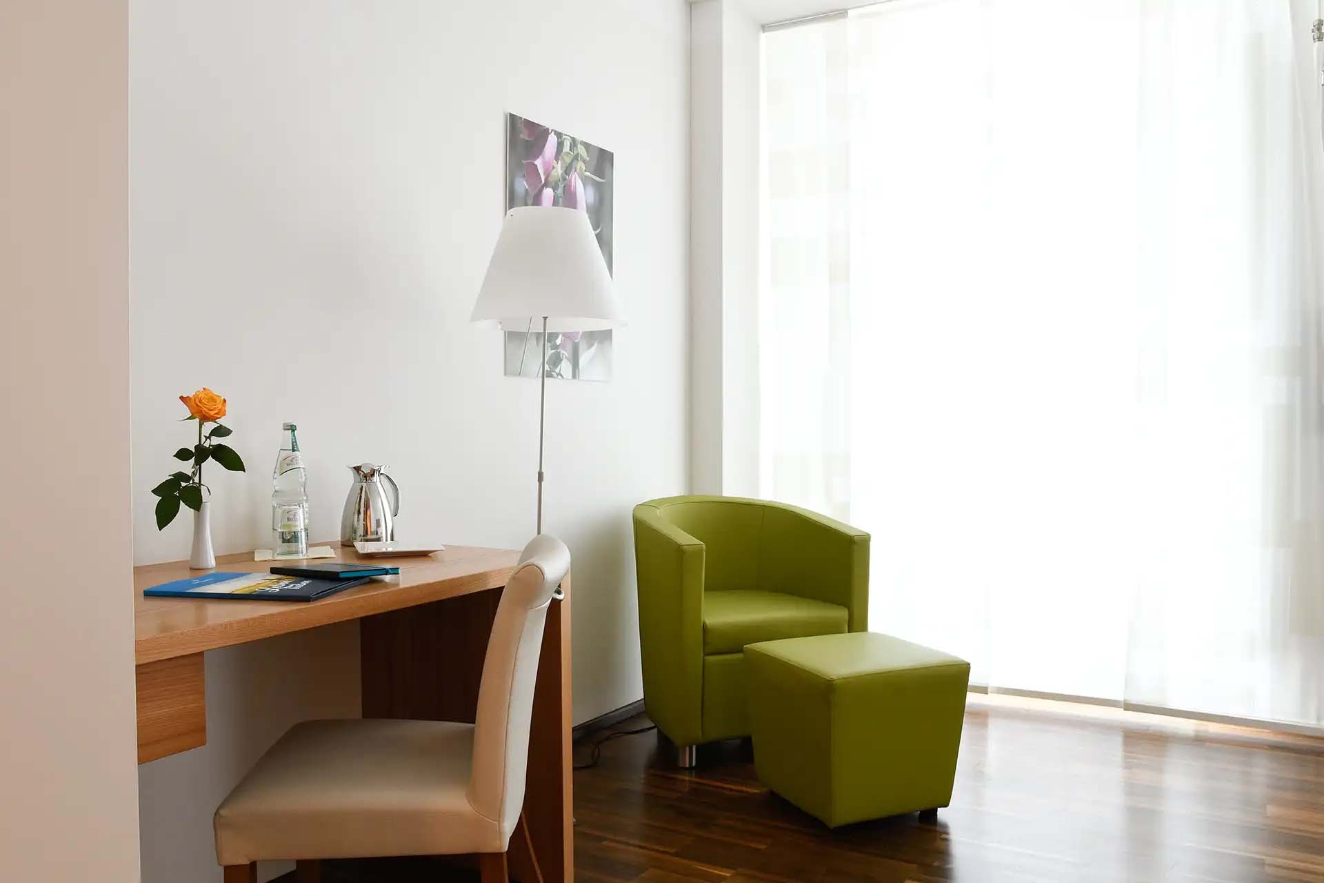 Helles Zimmer mit grünem Sessel, Schreibtisch und Blumendekoration.