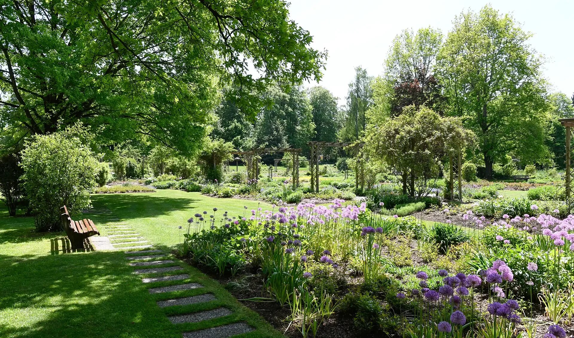 Blumenbeet und gepflasterter Weg im sonnigen Park mit Baenken.