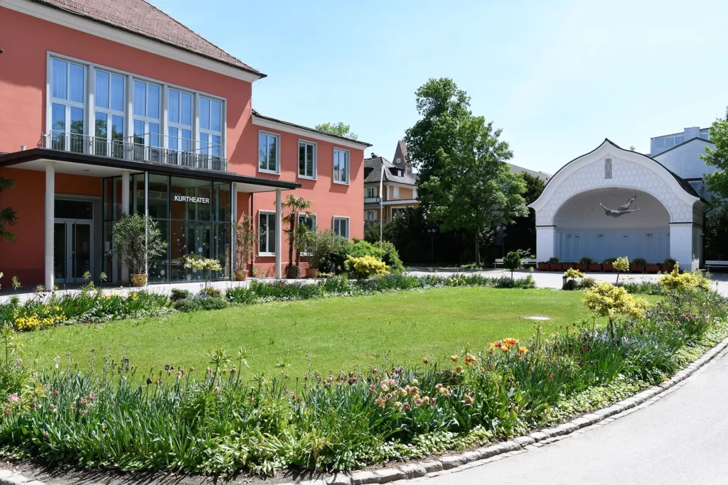 Kurtheater mit gepflegtem Garten und Springbrunnen im Sonnenschein.