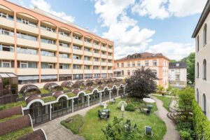 Hofansicht eines Gebaeudes mit Garten und Sitzgelegenheiten bei schoenem Wetter.