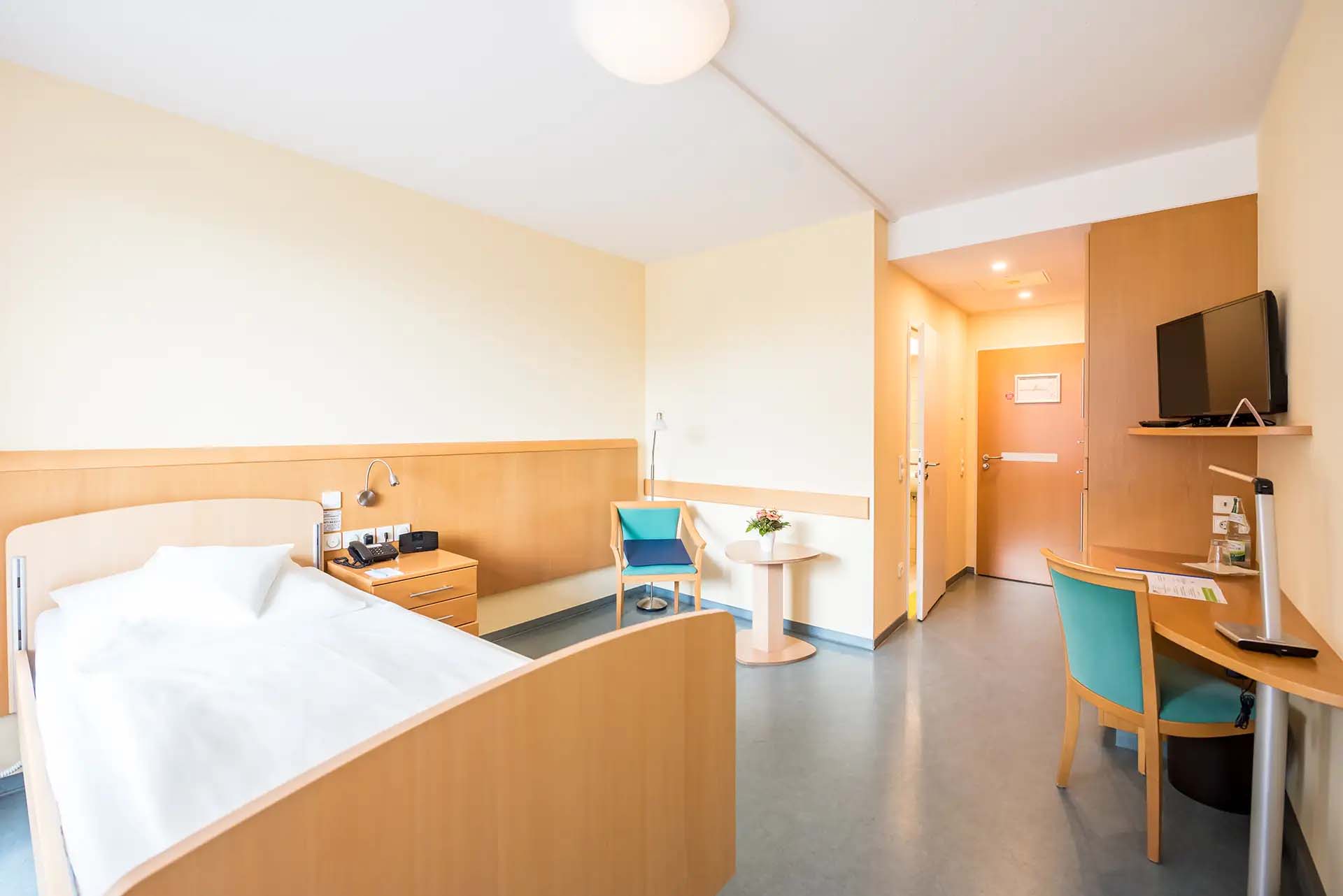 Modernes, gemuetliches Einzelzimmer mit Schreibtisch und Fernseher in heller Atmosphäre.