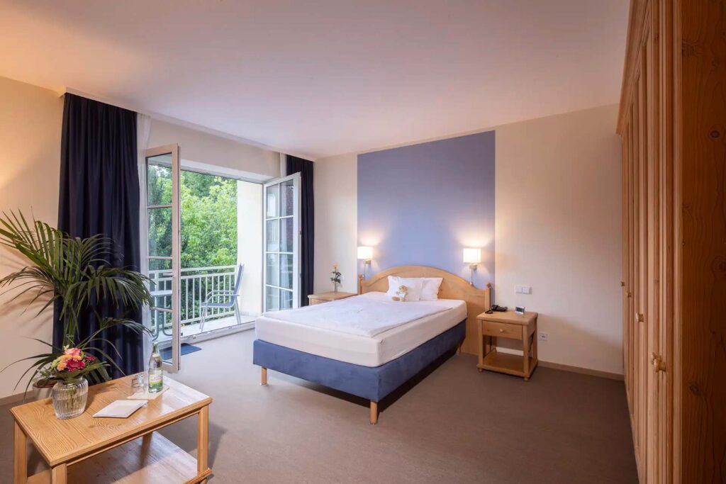 Gemütliches Patientenzimmer mit Doppelbett, Balkon und Blick ins Grüne.
