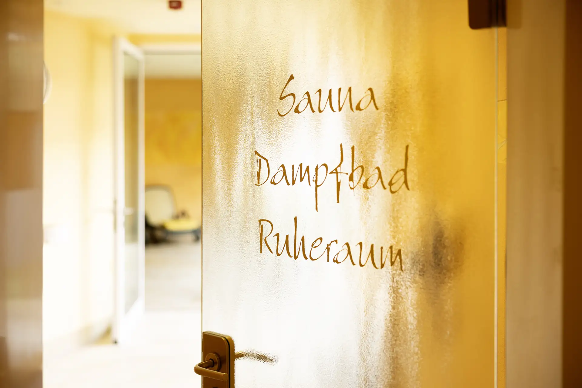 Beschriftete Glastür zu Sauna, Dampfbad und Ruheraum im Wellnessbereich.