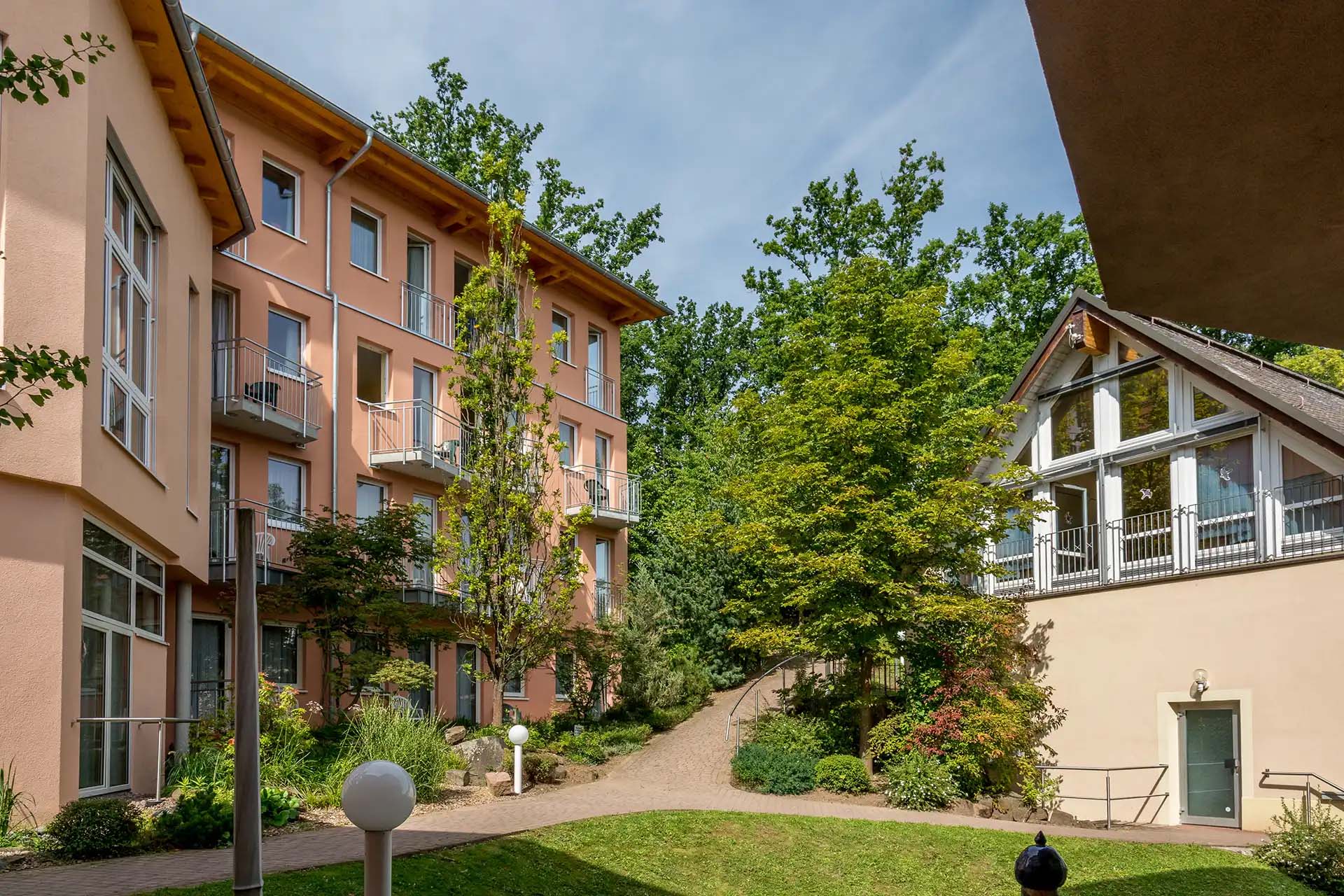 Klinikgebäude mit Balkonen und Glasfassade, umgeben von üppigem Grün.