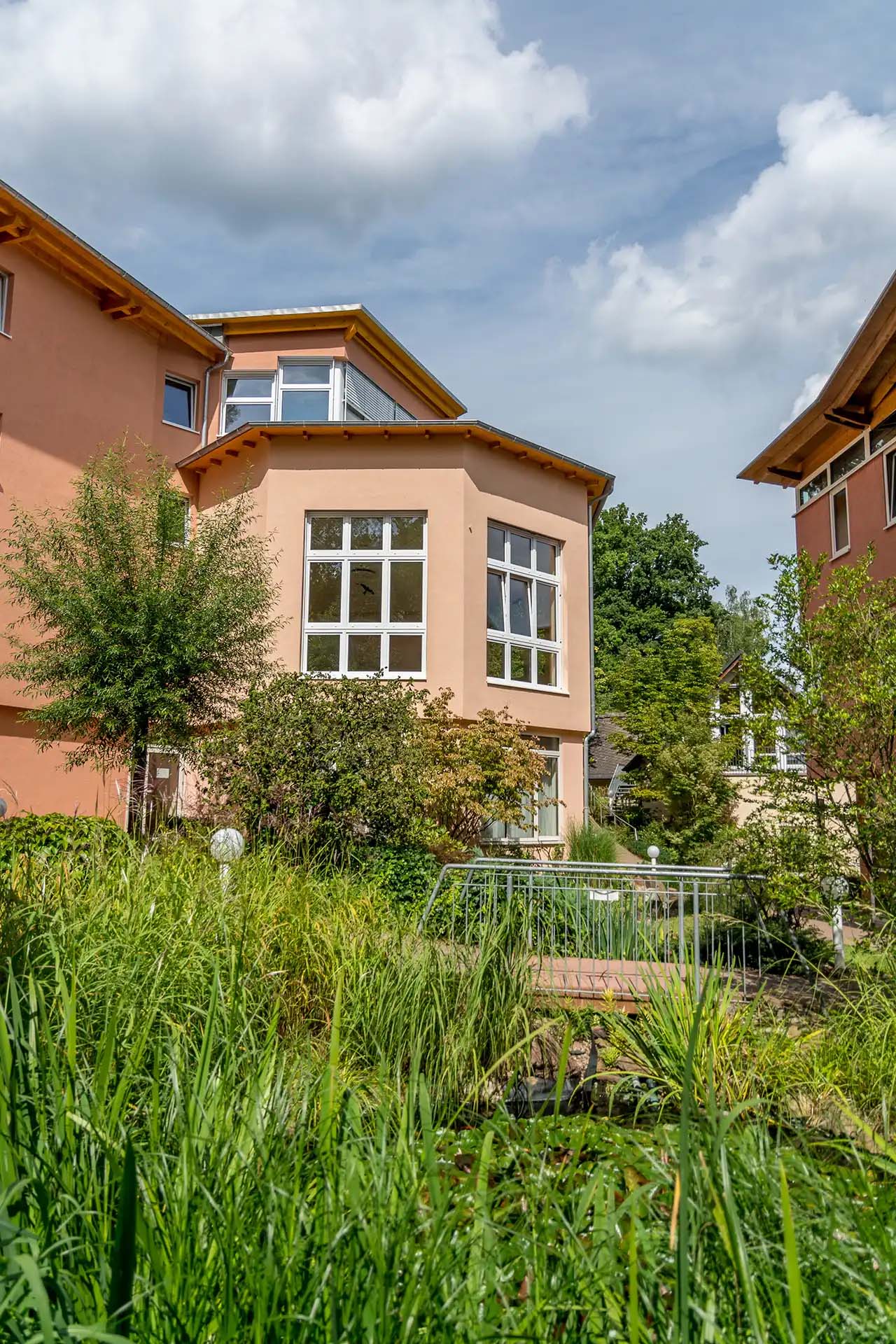 Klinikgebäude mit einem Wintergarten umgeben von üppigem grün.