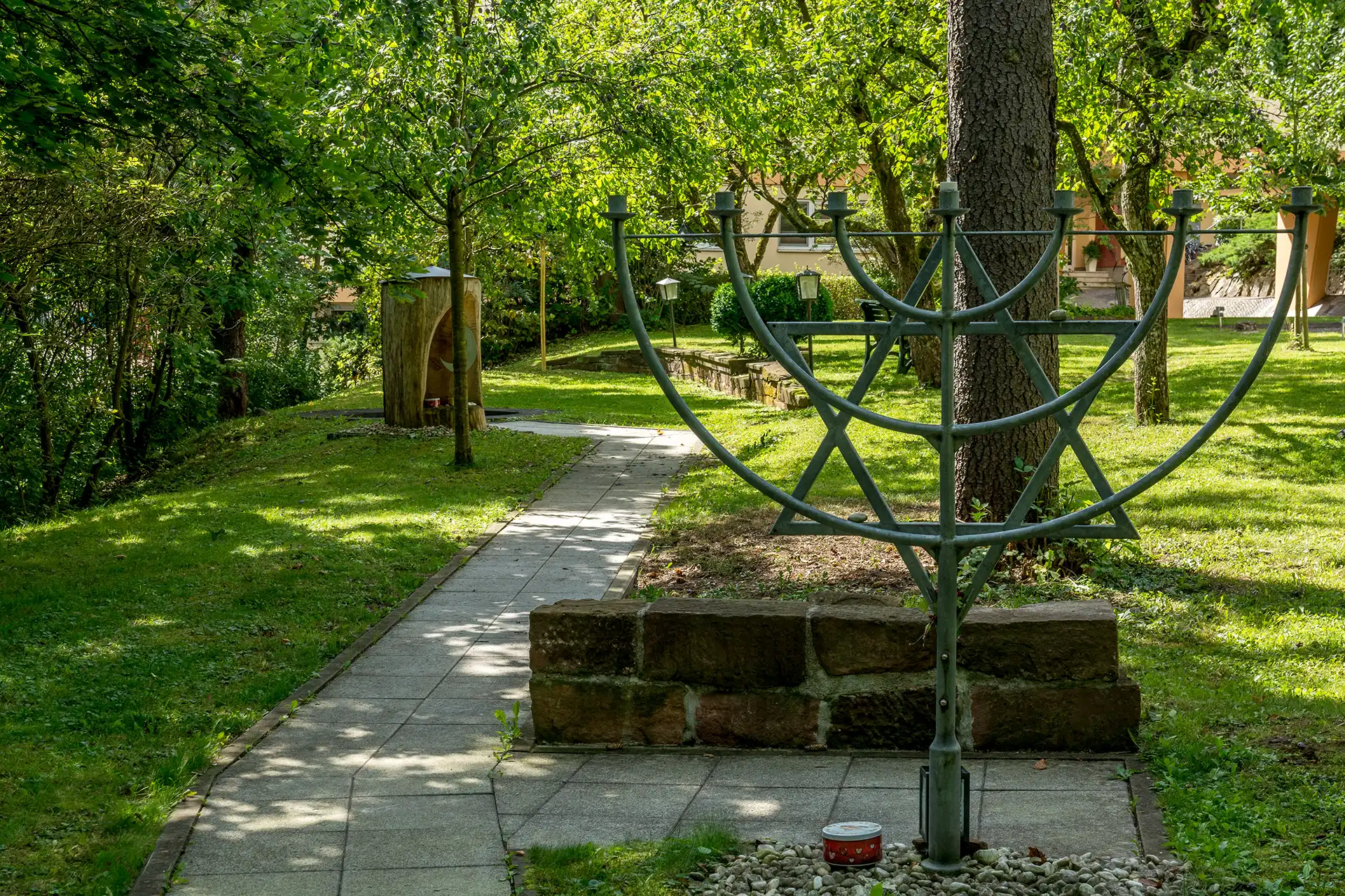 Kerzenstaender auf einem Weg im Park umsaeumt von Wiesen und Baeumen.