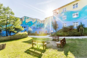 Farbenfrohes Gebäude mit Sonnenschein und Grünfläche im Vordergrund.