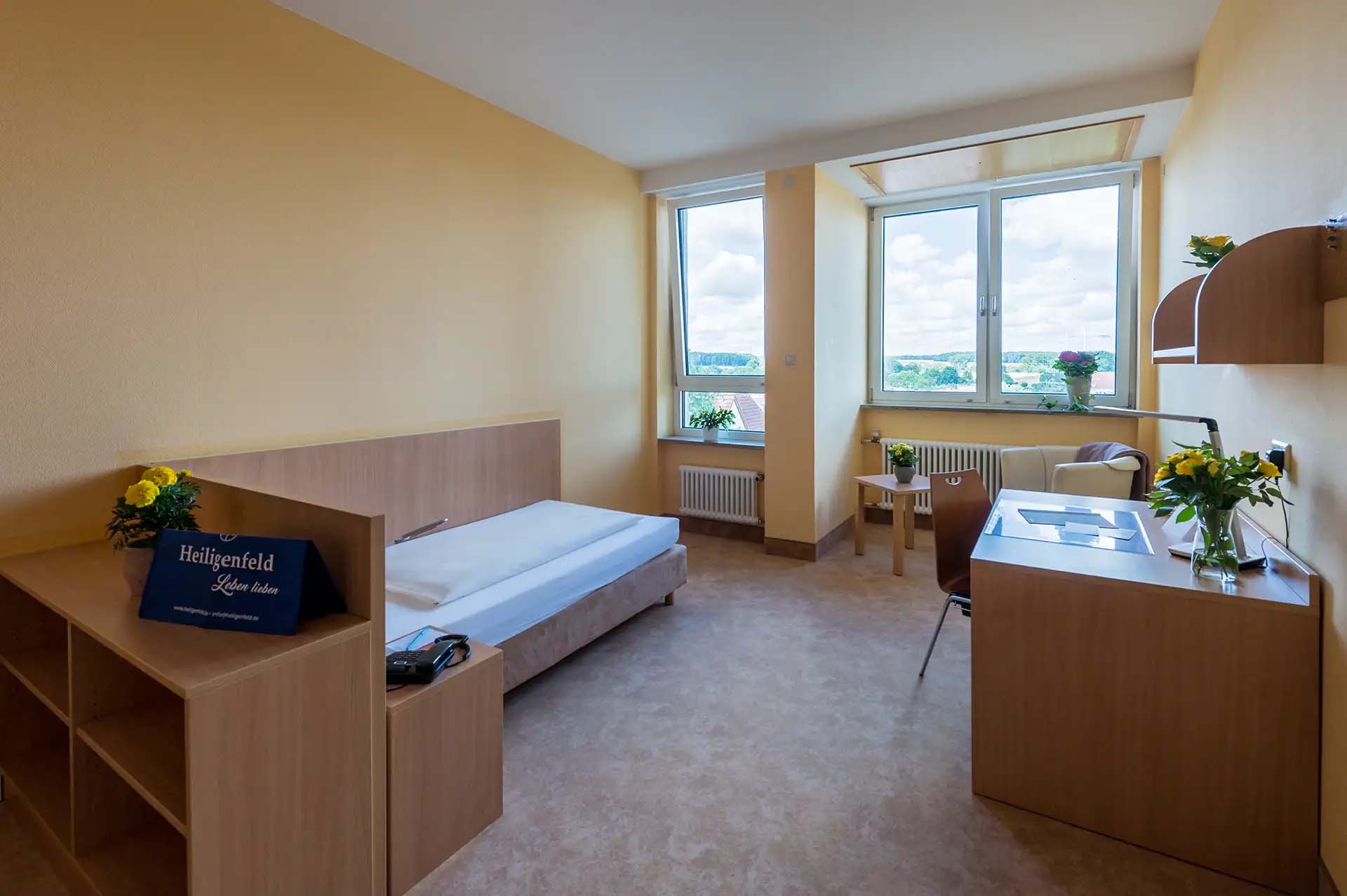 Geraeumiges Einzelzimmer mit Bett, Schreibtisch und großem Fenster mit Aussicht.