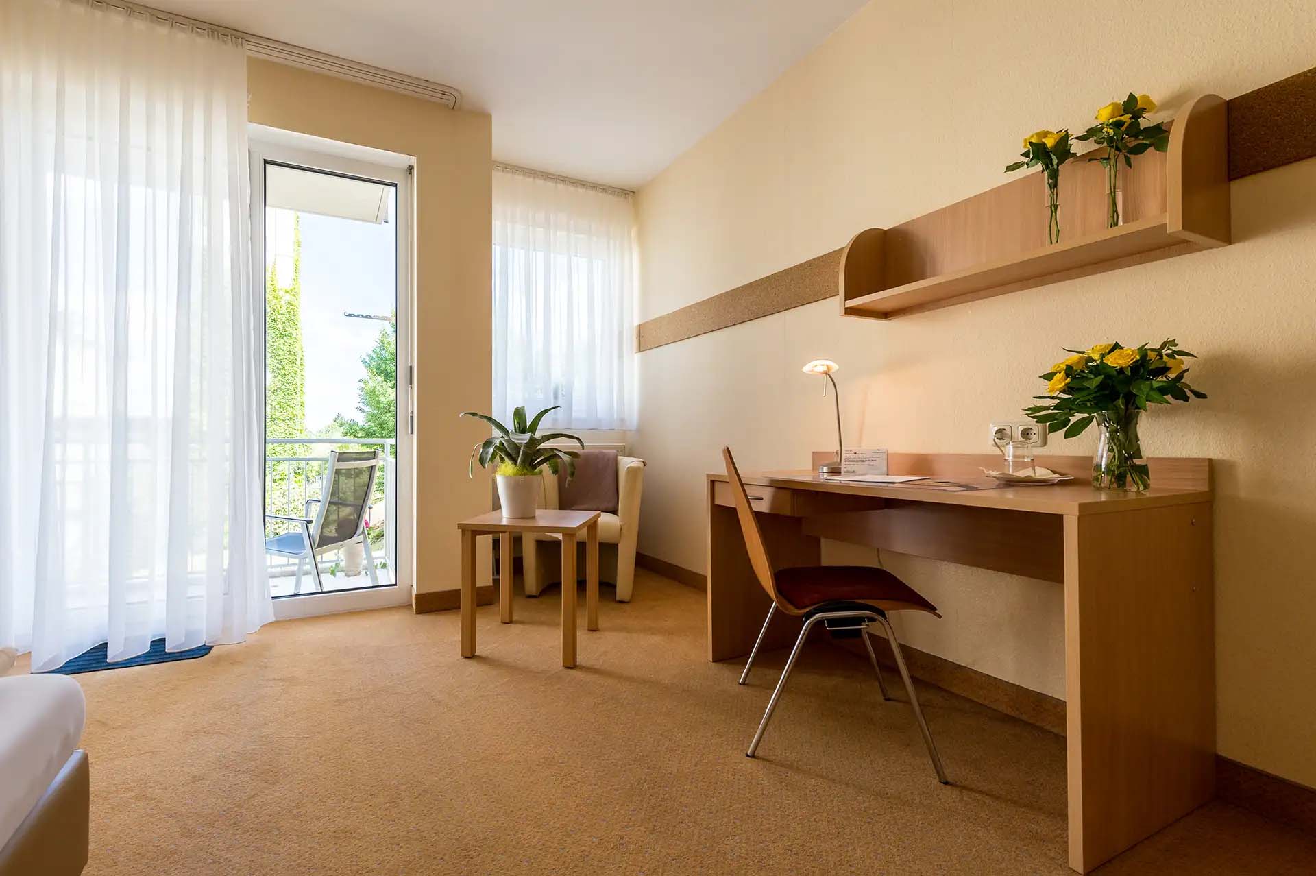 Einzelzimmer mit Schreibtisch, Stuhl, Pflanzen und Zugang zum Balkon.