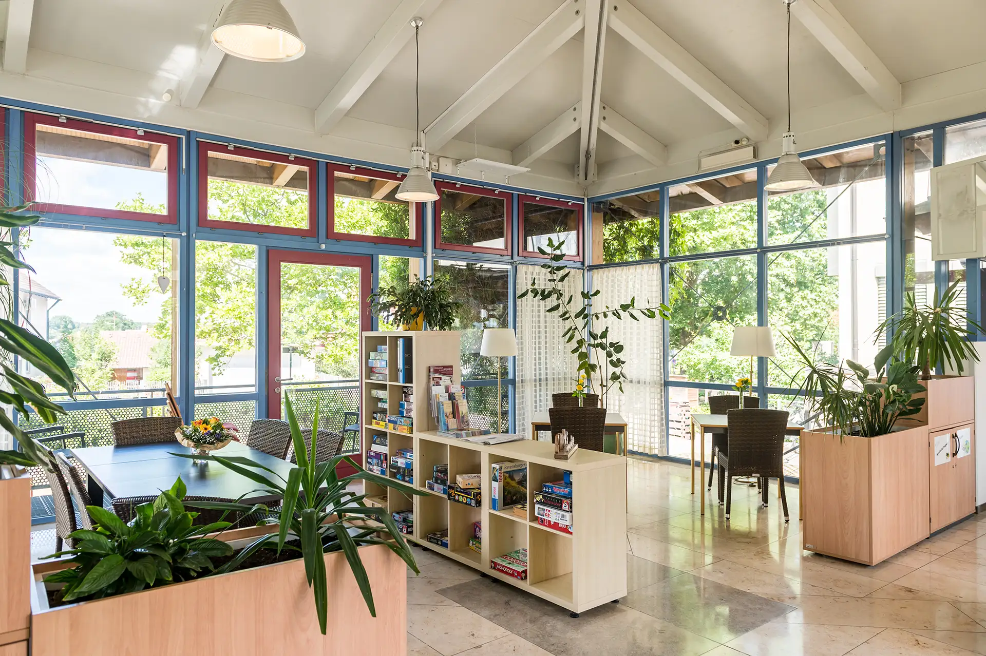 Helle Gemeinschaftslounge mit Pflanzen, Spielebibliothek und großen Fenstern.