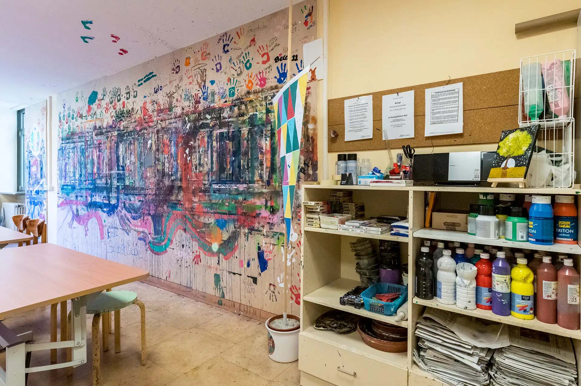 Kreativraum mit bemalter Wand und Regalen voller Kunstmaterialien.