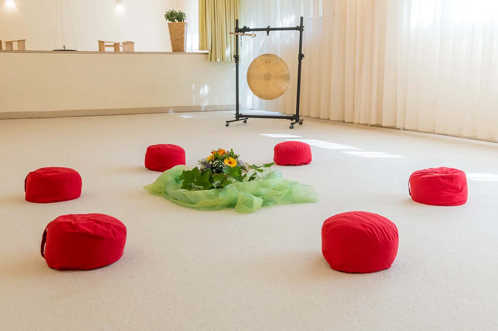 Meditationsraum mit roten Kissen, grünem Tuch und einer Gong im Hintergrund.