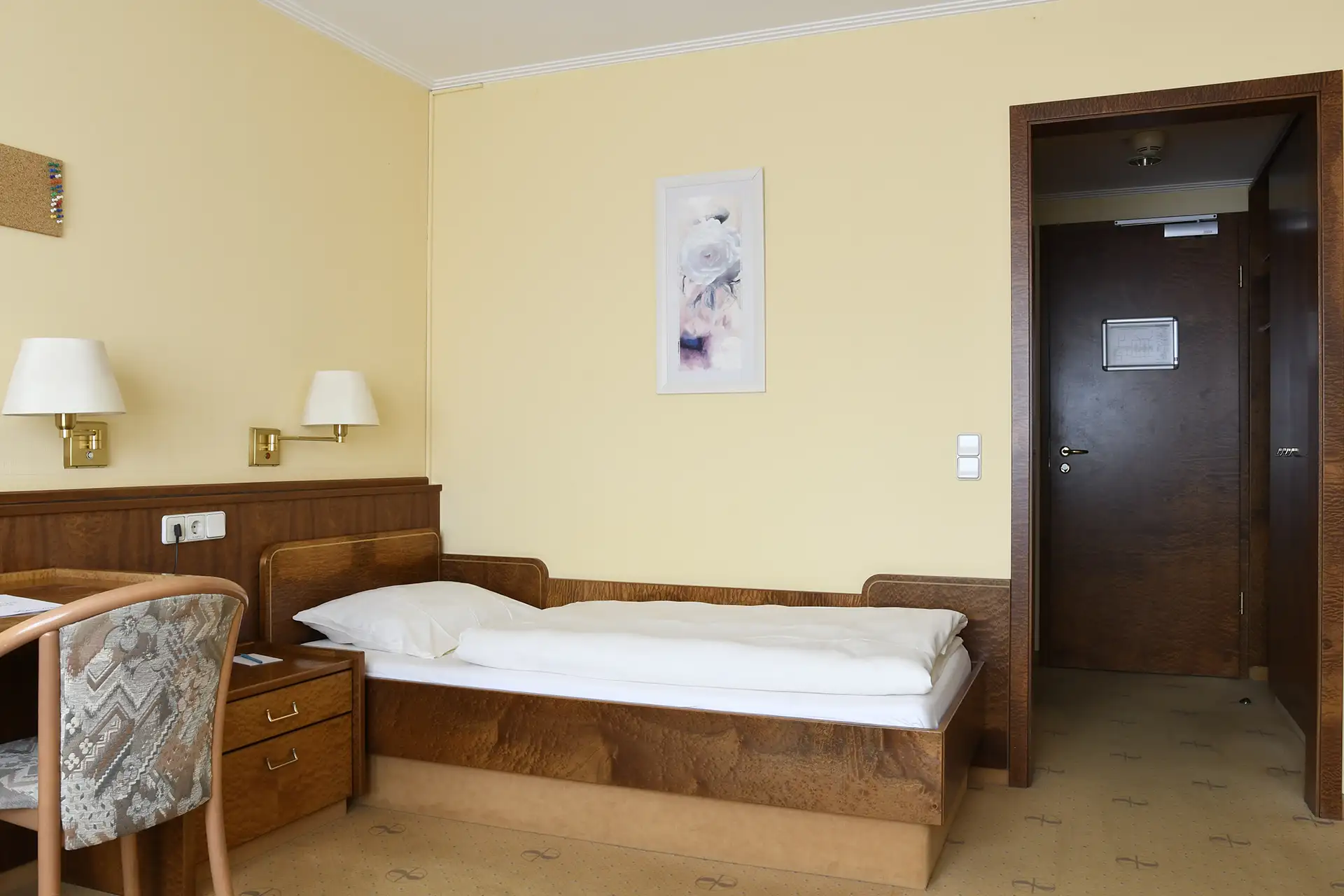Einzelzimmer mit Holzverkleidung, Bett, Schreibtisch und Stuhl in warmen Farben.