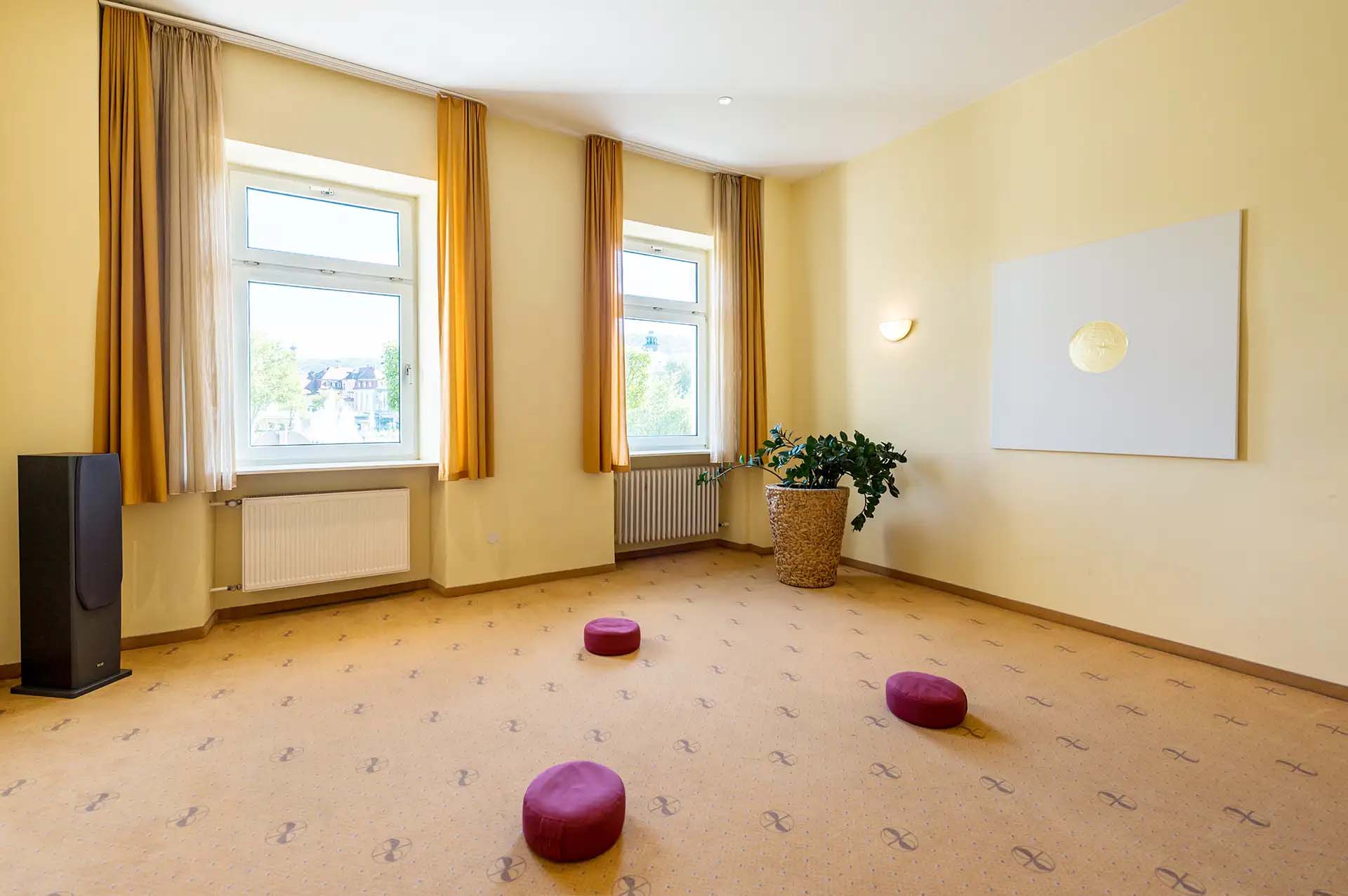 Meditationsraum mit Sitzkissen, großen Fenstern und entspannender Atmosphäre.