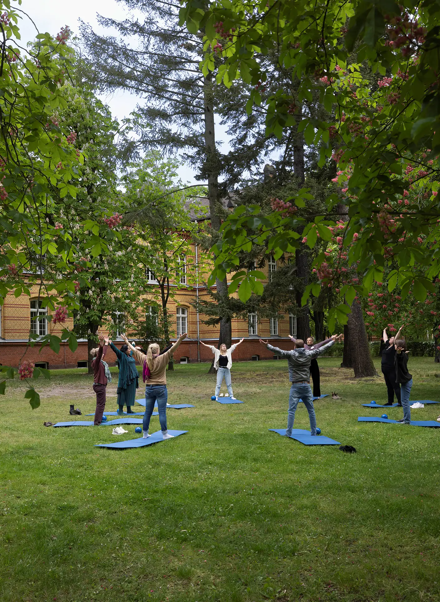 Gruppe bei Outdoor-Yoga-Session im Park vor einem Gebaeude.