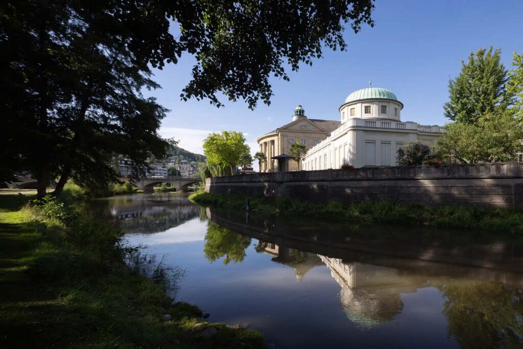 Klassizistisches Gebaeude mit Kuppel, reflektiert im ruhigen Fluss.