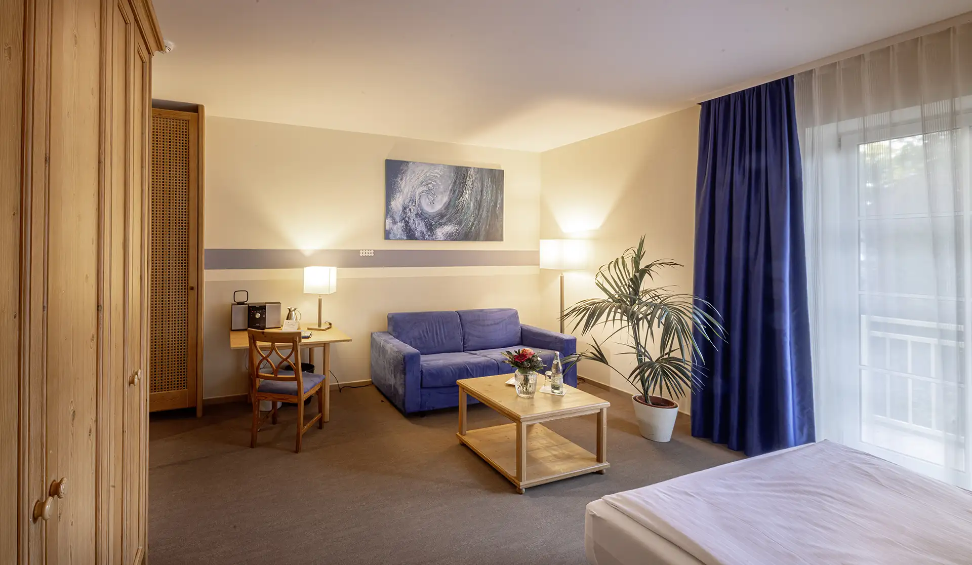 Gemütliches Patientenzimmer mit Sofa, Schreibtisch, und großen Fenstern.