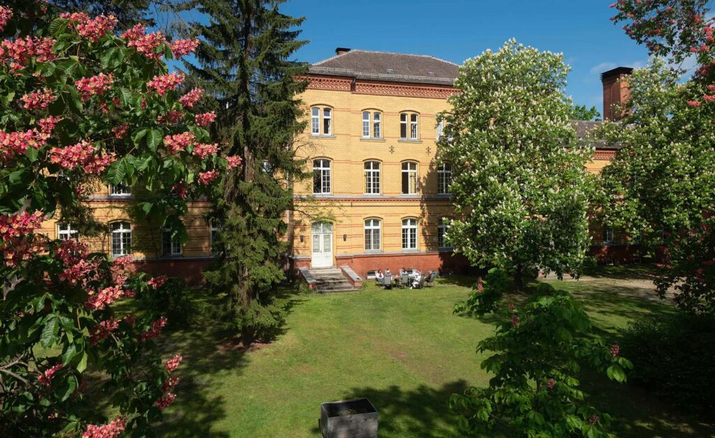 Historisches Gebäude mit blühenden Bäumen im Vordergrund an einem sonnigen Tag.