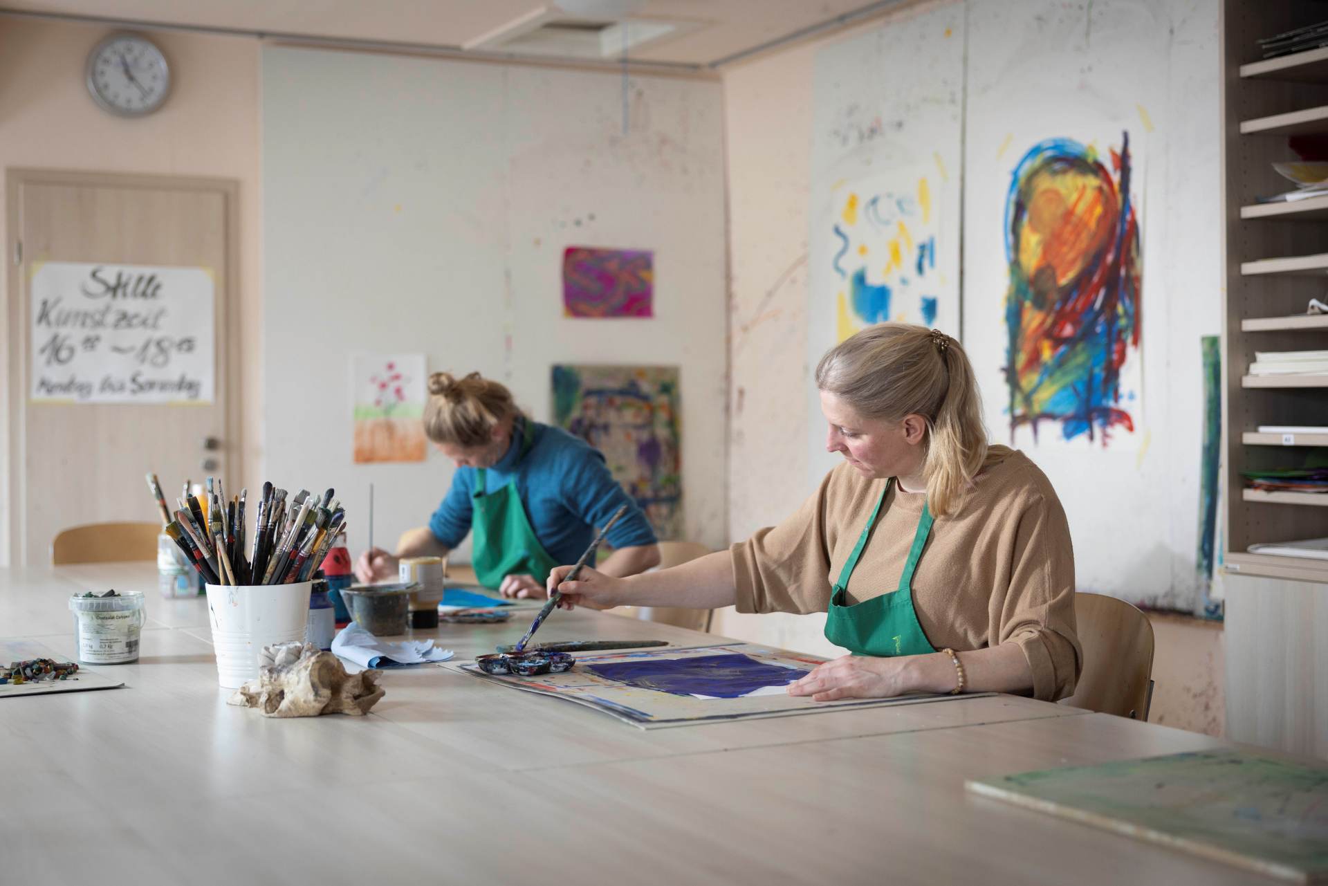 Patientinnen bei der Kunsttherapie im Malraum mit Pinsel und Farbe.