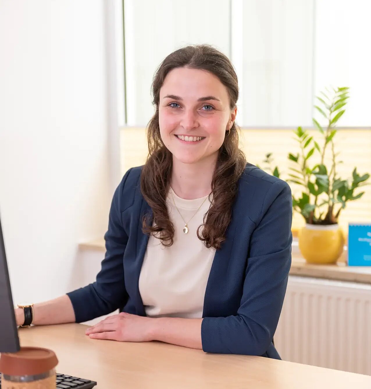 Frau am Schreibtisch mit Computer, Tasse und blauem Ordner.