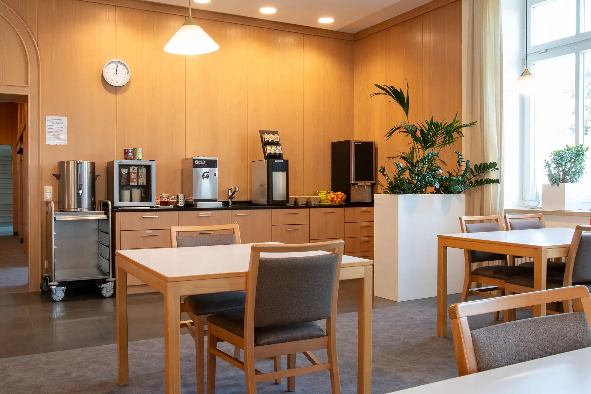 Gemütlicher Aufenthaltsraum mit Kaffeeautomaten, Tischen und Pflanzen für Pausen und Erholung.