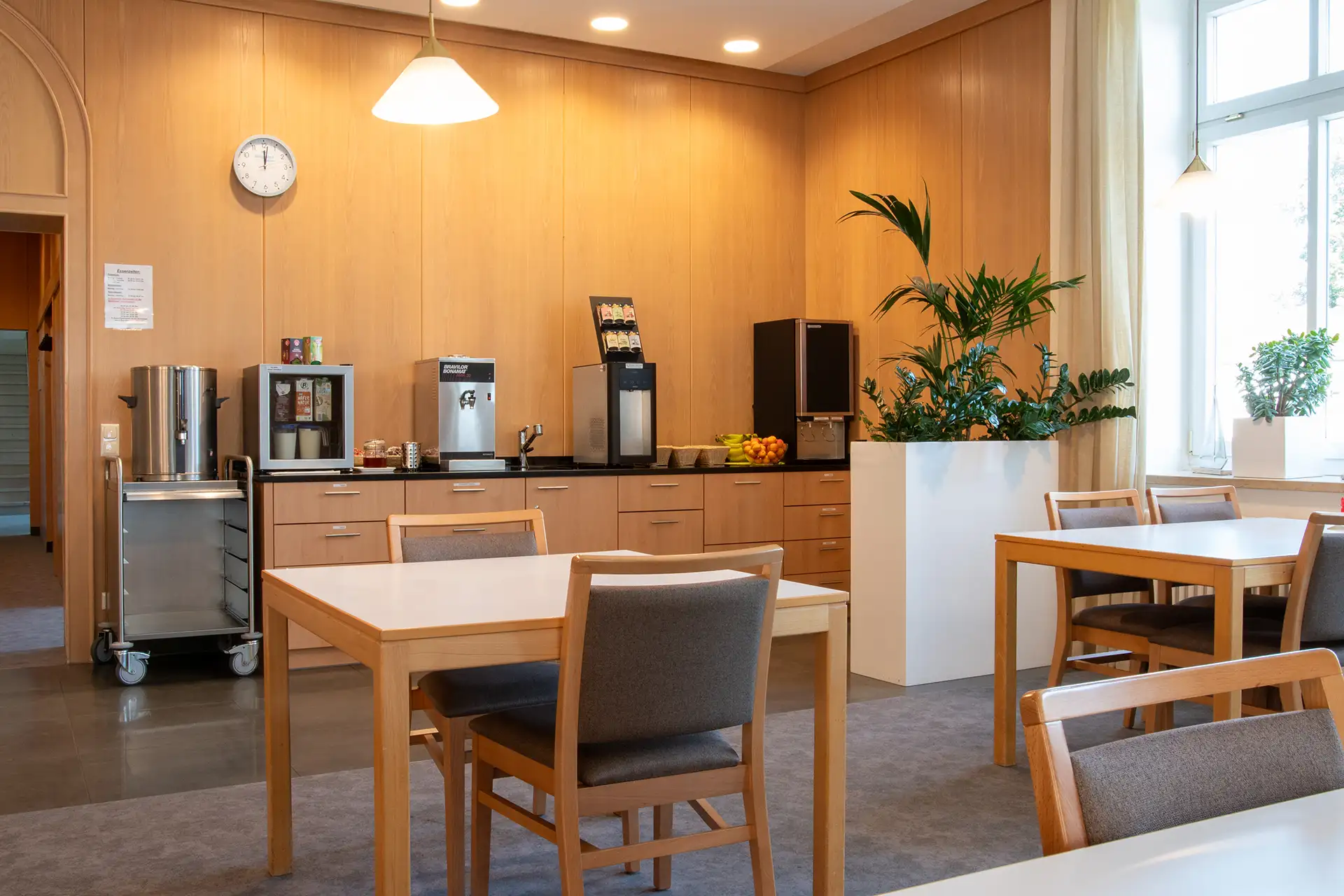 Gemütlicher Aufenthaltsraum mit Kaffeeautomaten, Tischen und Pflanzen für Pausen und Erholung.