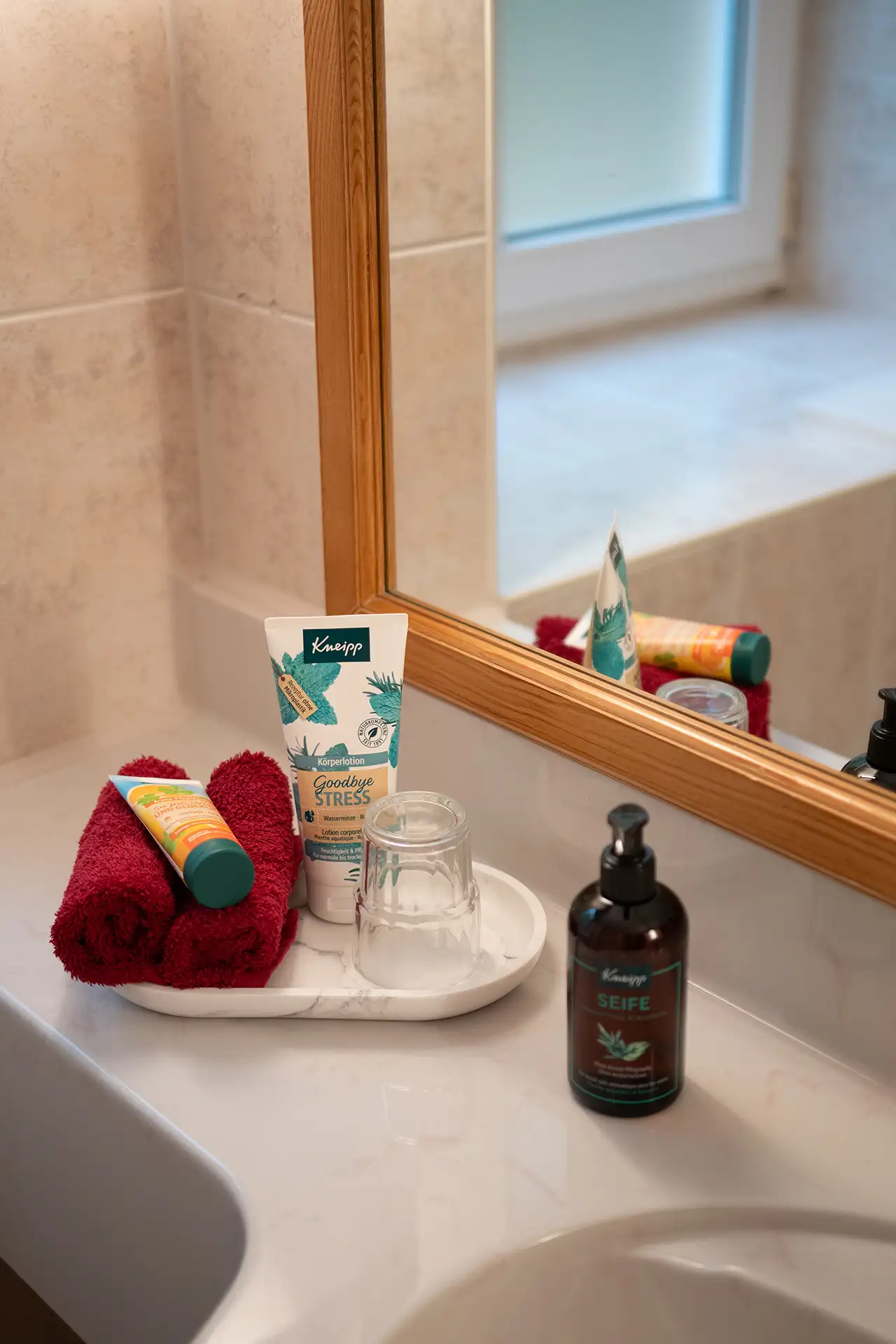 Badezimmerablage mit Handtuch, Pflegeprodukten, Glas und Seifenspender vor Spiegel.